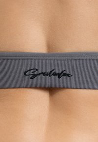 Grijze geribbelde band met zwart scriptlogo. De achtergrond toont een gladde huid, waardoor de textuur en het materiaal van de band worden benadrukt.
