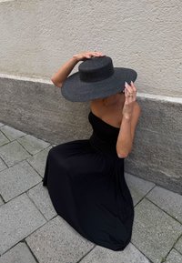 Črna brezramna maksi obleka z nabranim bodicem, teksturiran črn širok robnik in ozadje iz kamenčnih tlakovcev.