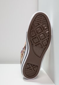 Hnědá gumová podrážka tenisky s bílým okrajem, vystavená geometrickým vzorem a logem Converse. Svršek ukazuje barevný, podrobný grafický design.