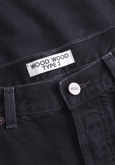 Mustad mustriga teksad, millel on silt tekstiga "WOOD WOOD TYPE 2." Omab metallist nuppu logoga ja kontrastset tikandit vöökohal.
