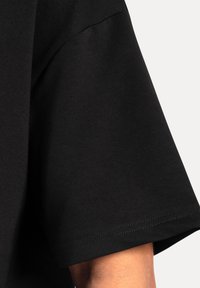 Camisa negra de manga corta hecha de algodón. La tela es suave con un ligero brillo. Presenta un cuello redondo y costuras reforzadas.