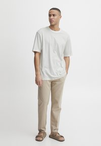 Short-sleeve, light grey crew-neck t-shirt paired with beige straight-leg pants and brown slide sandals, set against a white background.