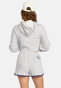 Grijze cropped hoodie met een verstelbare capuchon, gecombineerd met bijpassende grijze shorts met een marineblauwe rand en geborduurd logo aan de zijkant.