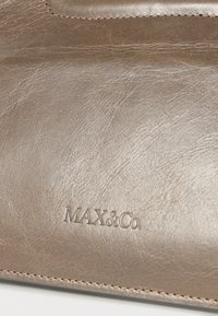 Δερμάτινο σε μεταλλικό ταουπέ με λεία υφή, που αναδεικνύει έντονα το ανάγλυφο λογότυπο της μάρκας "MAX&Co." και λεπτές ραφές.