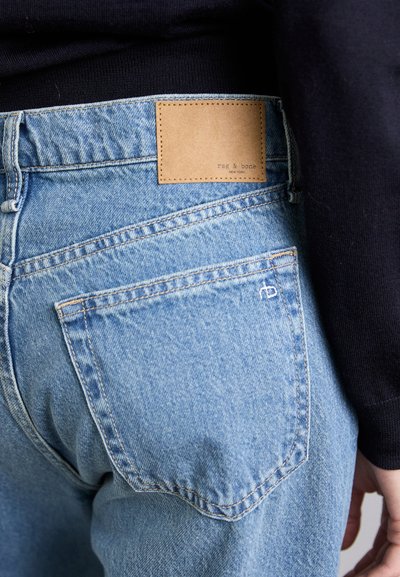 Ljusblå denimjeans har en brun läderlapp med text, bakfickor med förstärkta sömmar och en lätt blekt textur.