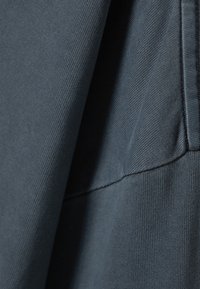 Tamno siva tkanina s teksturiranom površinom, koja prikazuje glatki, blago rastezljivi dizajn i vidljive detalje šavova.