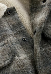 Wolljacke mit einem grau-beigen Farbschema, weichem Fleece-Futter, Druckknopfverschlüssen und zwei vorderen Taschen.
