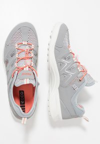 Scarpe sportive leggere grigie con tomaia in rete, accenti corallo a contrasto e suola in gomma bianca. Presentano lacci elastici e solette imbottite.