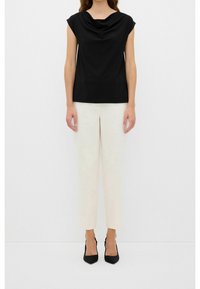 Top negro de cuello cisne con mangas tipo cap sleeve, combinado con pantalones de corte recto en beige claro, de largo hasta el tobillo, usados con tacones negros.