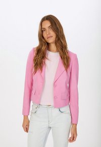 Pink cropped jacket with dual buttons, long sleeves, and notch lapels, layered over a light pink top. Worn with light distressed jeans.