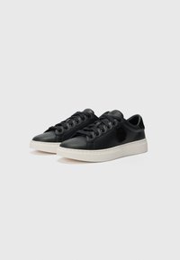 Sneaker in pelle nera con suole in gomma bianca, punta rotonda, sei asole, lacci piatti neri e un dettaglio testurizzato con il logo sul lato.