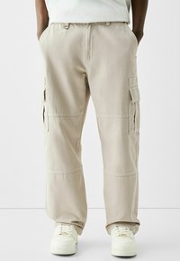 Beiga cargobyxor med fyra sidofickor, elastisk midja och förstärkt knäsydd, i kombination med vita sneakers.