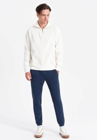Vit fleece-pullover med halv dragkedja, ihop med marinblå joggers med framfickor och sömnadsdetaljer, kompletterat med vita sneakers.