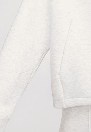 Lichtgrijze sweater met lange mouwen en zichtbare naaddetails en bijpassende lichtgrijze joggingbroek.