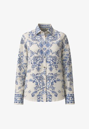 Blusa crema a maniche lunghe con intricati motivi floreali e paisley blu, davanti con bottoni, colletto appuntito e polsini decorati.