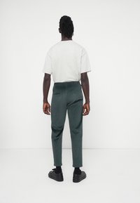 Grijze t-shirt met korte mouwen, gecombineerd met donkergroene corduroy broek met een elastische tailleband en zijzakken, gedragen met zwarte schoenen.