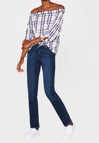 Helles karogemustertes Off-Shoulder-Oberteil in Weiß, Pink und Blau, kombiniert mit dunkelblauen Slim-Fit-Jeans und weißen Sneakers, was einen lässigen Look zeigt.