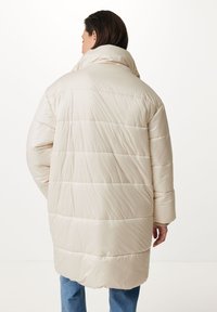 Abrigo acolchado color beige claro con cuello alto, mangas largas y costuras horizontales. Tejido suave y brillante con un corte relajado y longitud hasta la mitad del muslo.