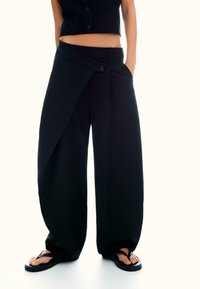 Zwarte wijde broek met een wikkelontwerp, voorzien van een enkele knoopsluiting en een soepele textuur. Gekocht met platte zwarte sandalen.