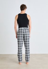Débardeur noir associé à un pantalon de pyjama à carreaux noir et blanc. Le pantalon a une taille élastique et une coupe décontractée.