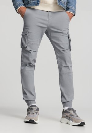 Pantaloni cargo grigi con gambe affusolate, polsini elastici e tasche laterali. Realizzati in tessuto morbido con cuciture visibili e una vestibilità morbida.
