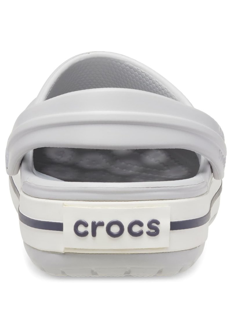 Zueco de goma gris con una correa cruzada trasera, plantilla texturizada y una banda blanca con una raya azul marino y el logo de "crocs".