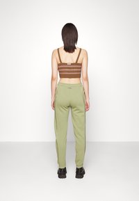 Brunrandig crop top med breda axelremmar, kombinerad med gröna sweatpants med sidostråk, fulländad med svarta kraftiga skor.