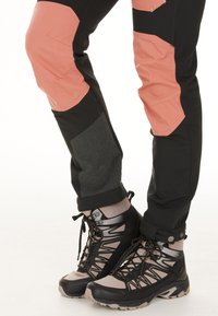 Zwarte hikingbroeken met roze accenten en gestructureerde knieën, gecombineerd met zwart-grijze wandelschoenen met ingewikkelde veters en rubberen zolen.