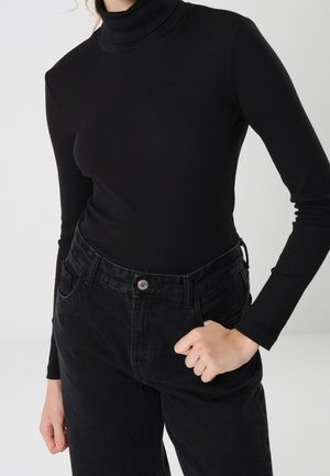 Osoba ubrana w czarny prążkowany long sleeve golf, włożony do wysokich czarnych jeansów z przednim zapięciem na guziki i szlufkami na pasek.
