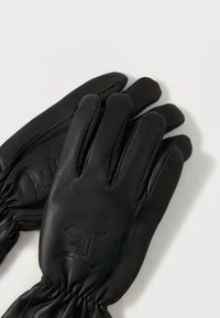 Een paar zwarte leren handschoenen met elastische polsen en reliëf gestileerde logo's op de achterkant van beide handen, plat gelegd op een witte ondergrond.