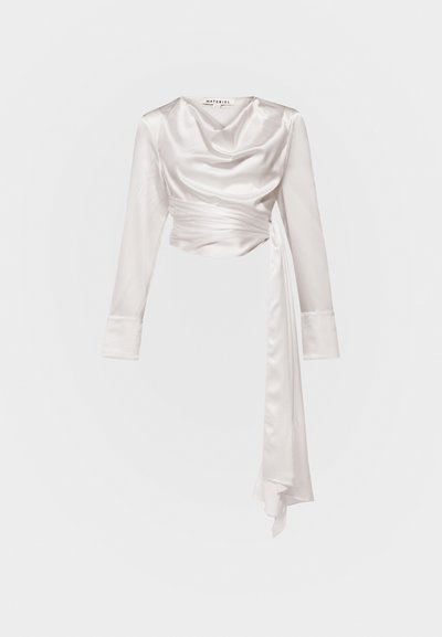 Top από σατέν φινίρισμα, ελεφαντόδοντου, με μακριά μανίκια, draped neckline και λεπτομέρεια στη μέση που δένει. Λείο υλικό με διακριτική λάμψη.