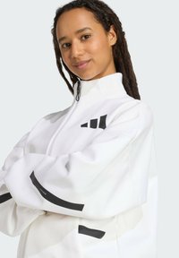 White zip-up jacket with black accents, featuring a stand-up collar and sleek design. Smooth texture with horizontal stripes on sleeves.