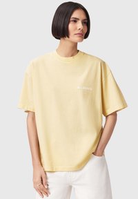 Κίτρινο βαμβακερό T-shirt με άνετη εφαρμογή, κοντά μανίκια και στρογγυλή λαιμόκοψη· διαθέτει μικρό λευκό λογότυπο στο μπροστινό μέρος.