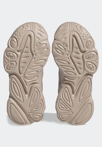 Ljust beige sneaker-sulor med en texturerad gummidesign och upphöjda mönster och fåror för grepp och stöd, märkta med logotypen.