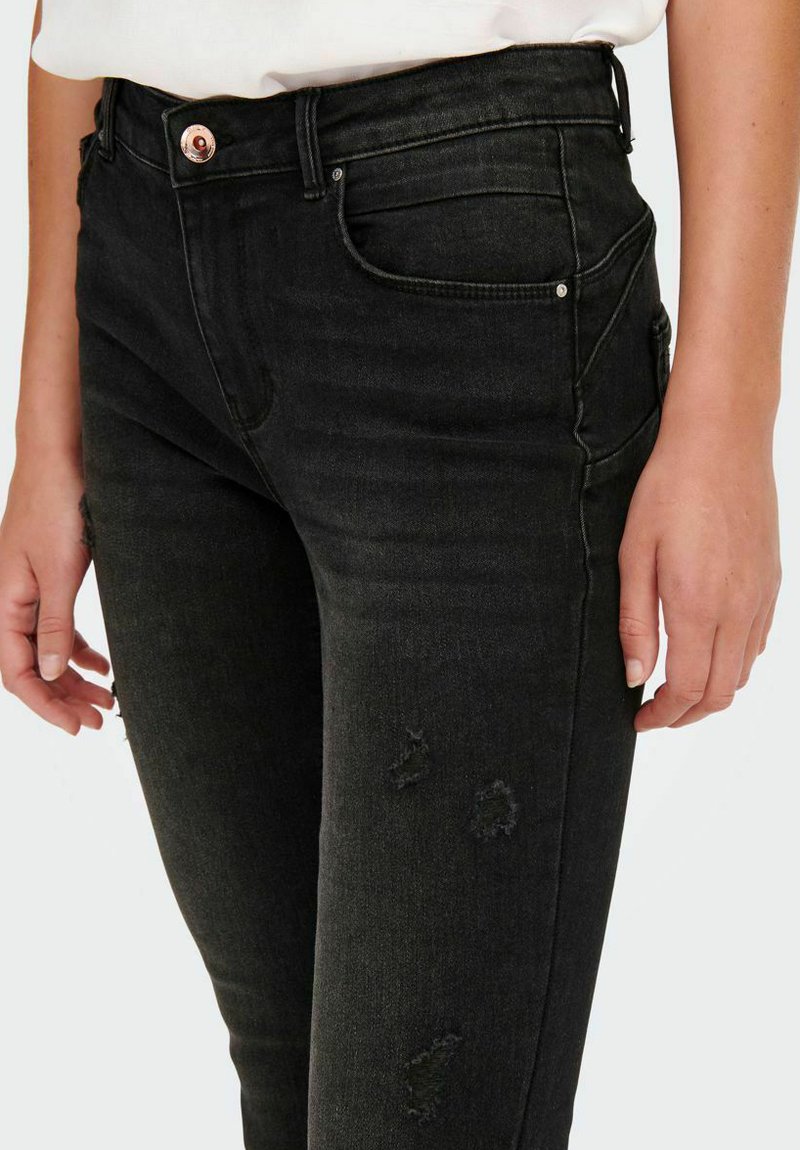Jean en denim noir avec taille haute, coupe ajustée, détails déchirés et un bouton en bronze à la taille. Quatre poches visibles.