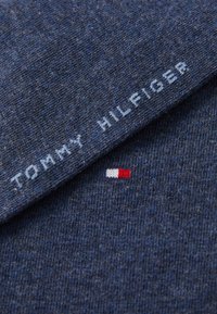 Kék kötött anyag texturált felülettel. Fehér "TOMMY HILFIGER" felirat és egy kis piros, fehér és kék logó részlet található rajta.