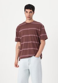 Brown striped t-shirt with short sleeves, round neckline, and a relaxed fit. Fabric is cotton; stripes are in a lighter shade of pink.