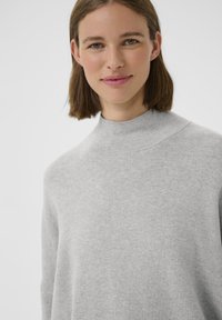 Maglione grigio a coste con collo alto e vestibilità rilassata. Presenta maniche lunghe e una texture morbida e liscia. Nessun motivo o accessorio visibile.