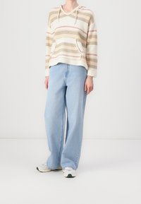 Sweat à capuche rayé en crème, beige et rose avec une poche kangourou, associé à un jean large bleu clair et des baskets grises.