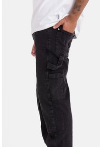 Pantalones cargo negros de corte ajustado, hechos de denim. Presentan bolsillos laterales, detalles de costura y una textura cepillada.