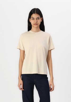 Beige katoenen t-shirt met een ronde hals, korte mouwen en een relaxte pasvorm, gecombineerd met donkere denim jeans. Soepele textuur, minimalistisch ontwerp.