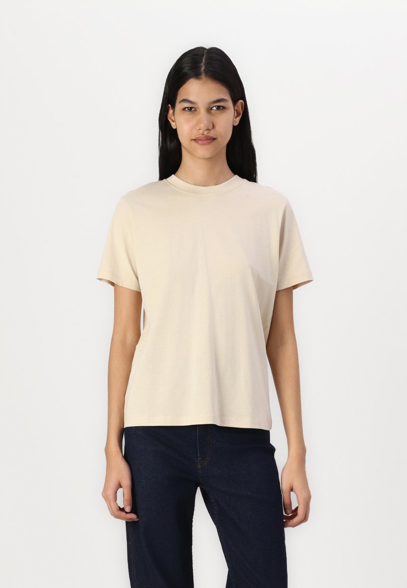 Beige bomull t-skjorte med rund hals, korte ermer og en avslappet passform, kombinert med mørke denimjeans. Glatt tekstur, minimalistisk design.