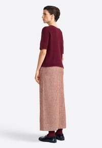 Burgundy short-sleeve knit top paired with a long, textured cream and orange checkered skirt, finished with black shoes and matching socks.