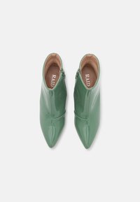 Botas de tobillo de charol verde con punta afilada, que cuentan con un cierre de cremallera lateral y un diseño minimalista. El interior tiene un forro marrón.