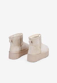 Beżowe zamszowe botki za kostkę z miękką wyściółką, płaską podeszwą i małym uchwytem z tyłu. Charakteryzują się lekko teksturowaną powierzchnią.