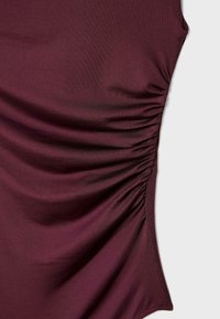 Burgundy topp i glatt tyg, med sidoskräddning och en smal passform. Ingen synlig hårdvara eller mönster.