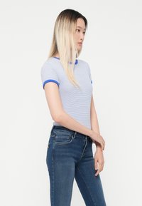 Ριγέ κοντομάνικο μπλουζάκι σε ανοιχτό μπλε και λευκό, με μπλε αντίθεση στον λαιμό και τις άκρες των μανικιών, συνδυασμένο με σκούρα μπλε τζιν.