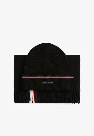 Ensemble bonnet en tricot noir et écharpe assortie. L'écharpe est ornée de franges à pompons. Le bonnet a une bande contrastante et une étiquette de logo. Tissu texturé.