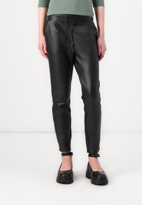 Svarte skinnbukser med tapered fit, elastisk midjebånd og snøring. Har ankelglidelåser og glatt tekstur.