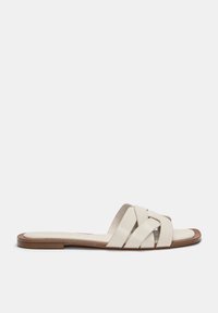 Sandales glissantes en cuir blanc avec un design de lanière croisée, semelle plate et un accent en bois clair sur le bord. Texture lisse, style minimaliste.